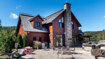 A large wooden house with a stone chimney, outdoor seating, and a swimming pool.