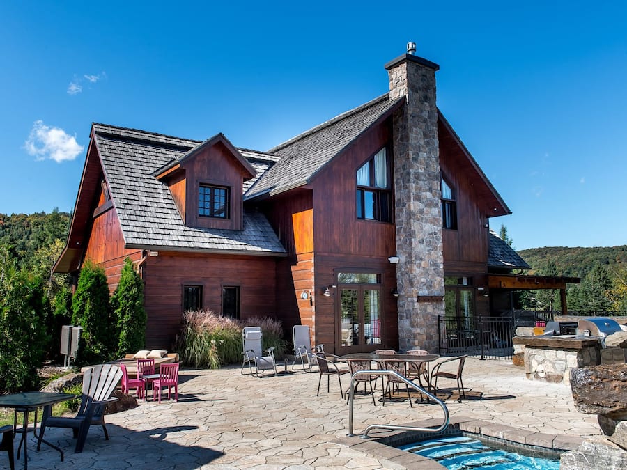 A large wooden house with a stone chimney, outdoor seating, and a swimming pool.