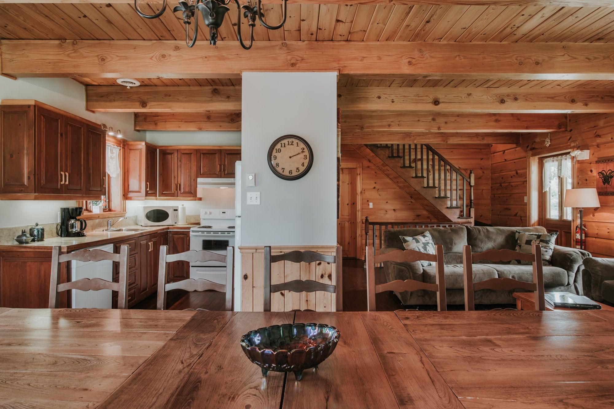 A wooden interior with a dining table, chairs, a kitchen area, and a staircase.