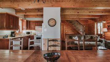 A wooden interior with a dining table, chairs, a kitchen area, and a staircase.