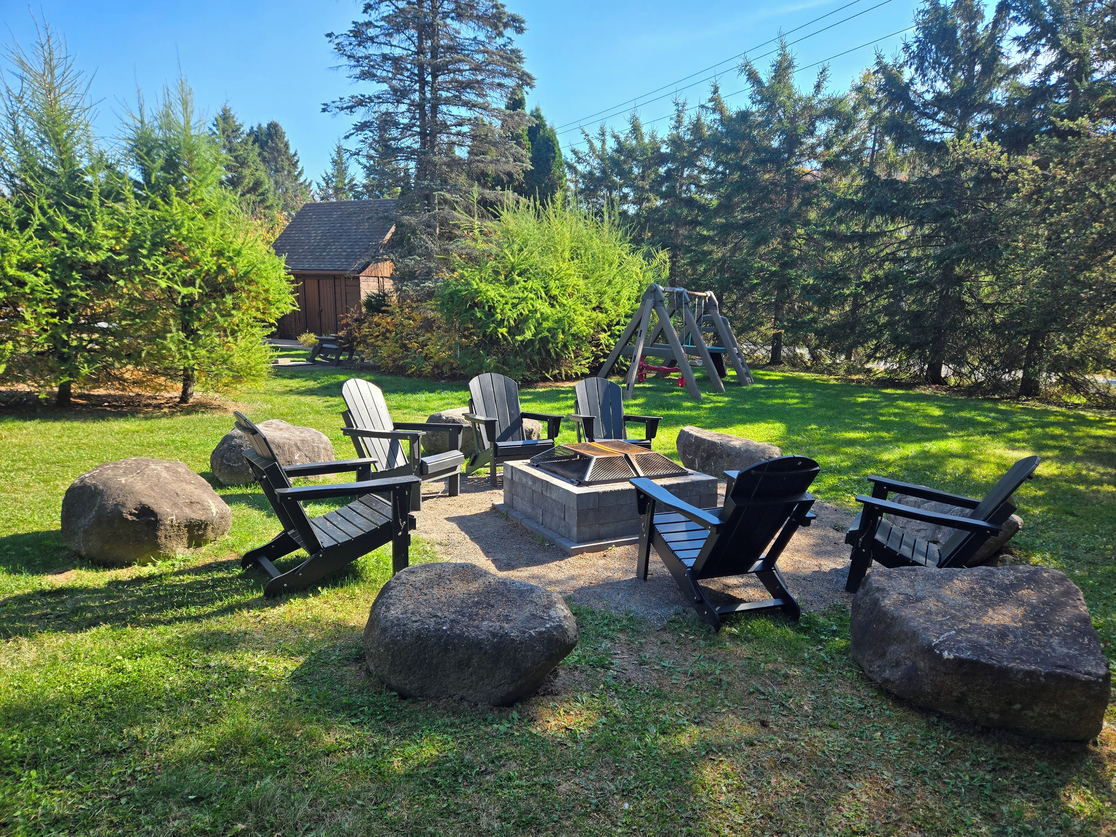 Ein Garten mit Adirondack-Stühlen, einer Feuerstelle und einer Schaukel.