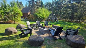 A backyard with Adirondack chairs, a fire pit, and a swing set.