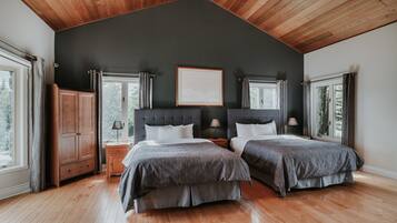 A bedroom with two beds, wooden flooring, a dark ceiling, and large windows.
