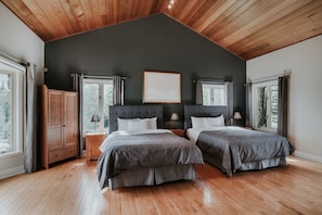 A bedroom with two beds, wooden flooring, a dark ceiling, and large windows. - Chalets Royal Laurentien (Mont-Blanc)