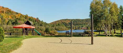 Un parque con zona de arena, parque infantil, pabellón cubierto y lago.