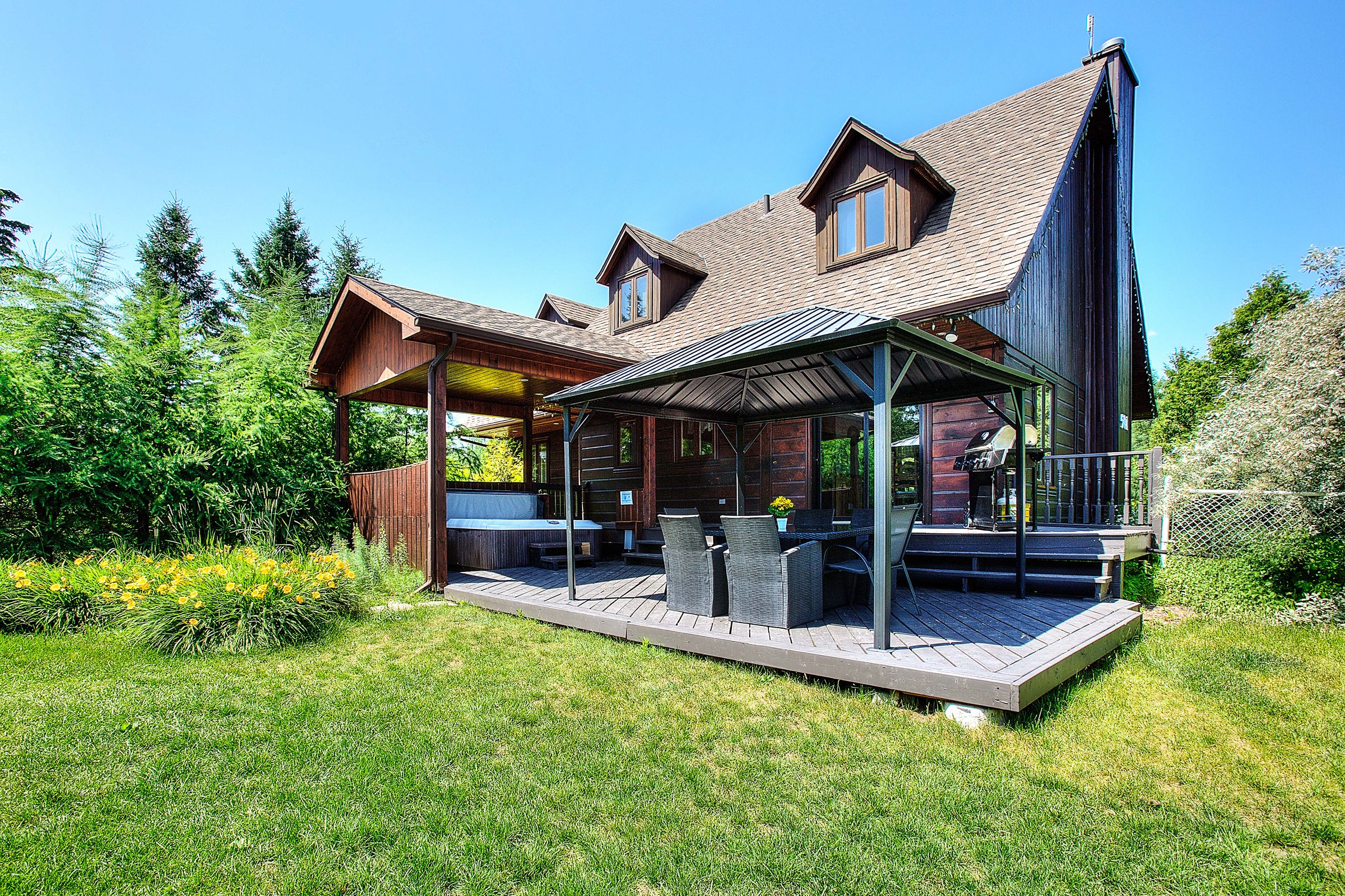Ein zweistöckiges Holzhaus mit überdachter Terrasse, Whirlpool und Grill.