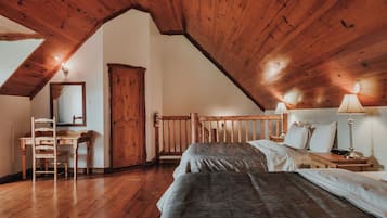 Une chambre confortable située dans les combles, avec un plafond en bois incliné, un bureau en bois avec une chaise, un lit avec du linge de lit blanc et une table de chevet avec une lampe.