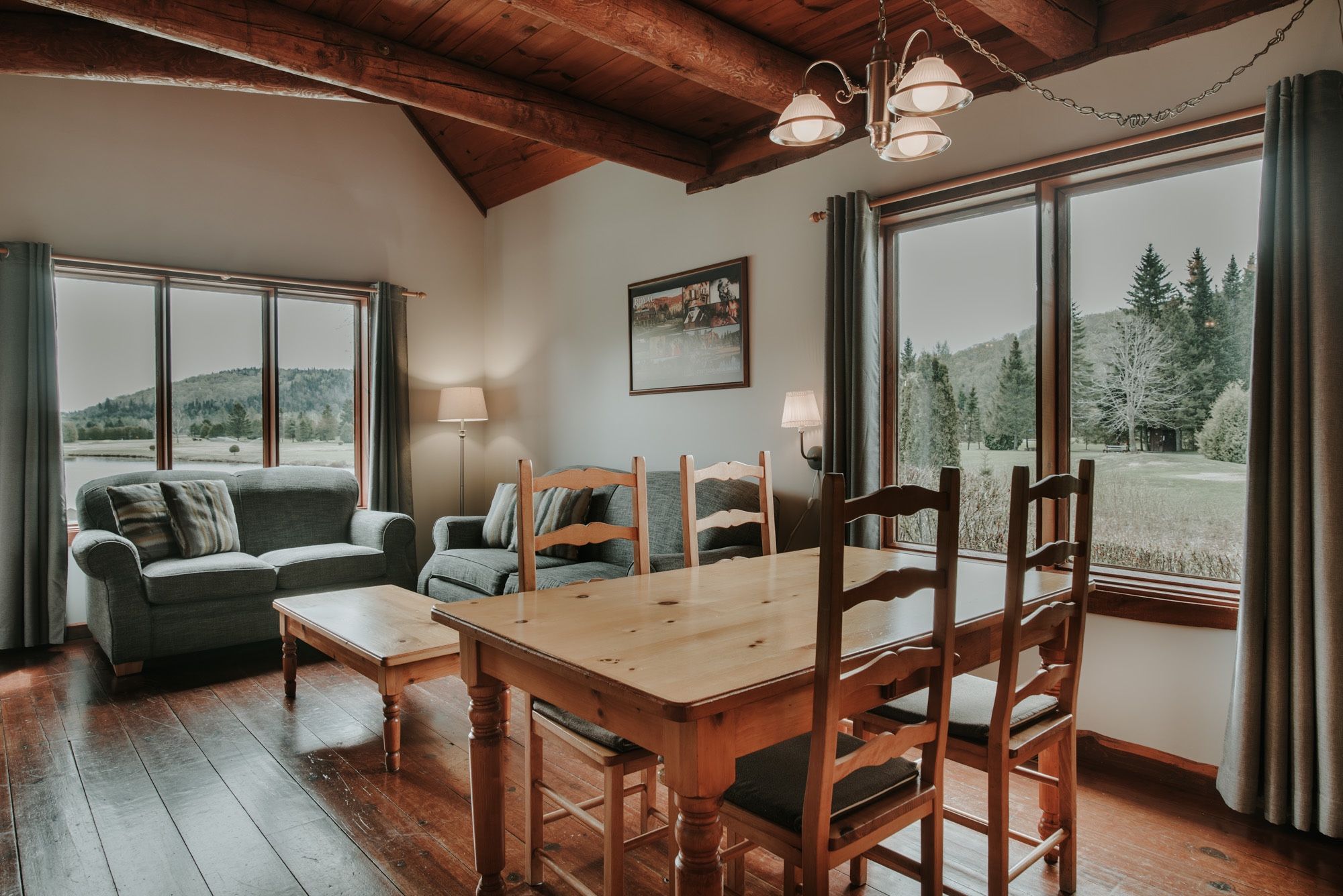 A cozy room with a wooden dining table, two sofas, and a large window with a view of trees and hills.