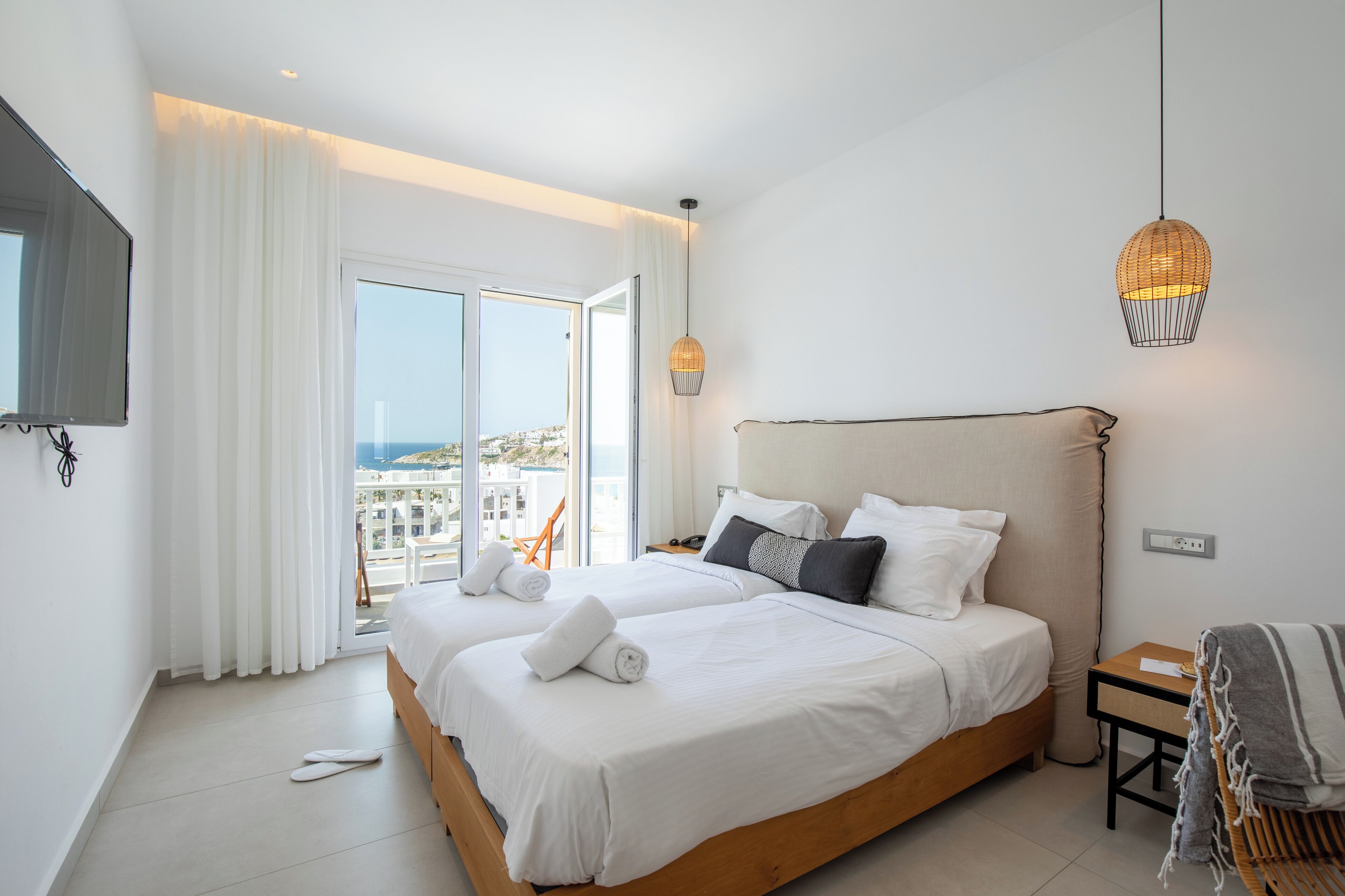 Habitación de hotel con dos camas, un ventanal con cortinas, un televisor y una lámpara colgante.