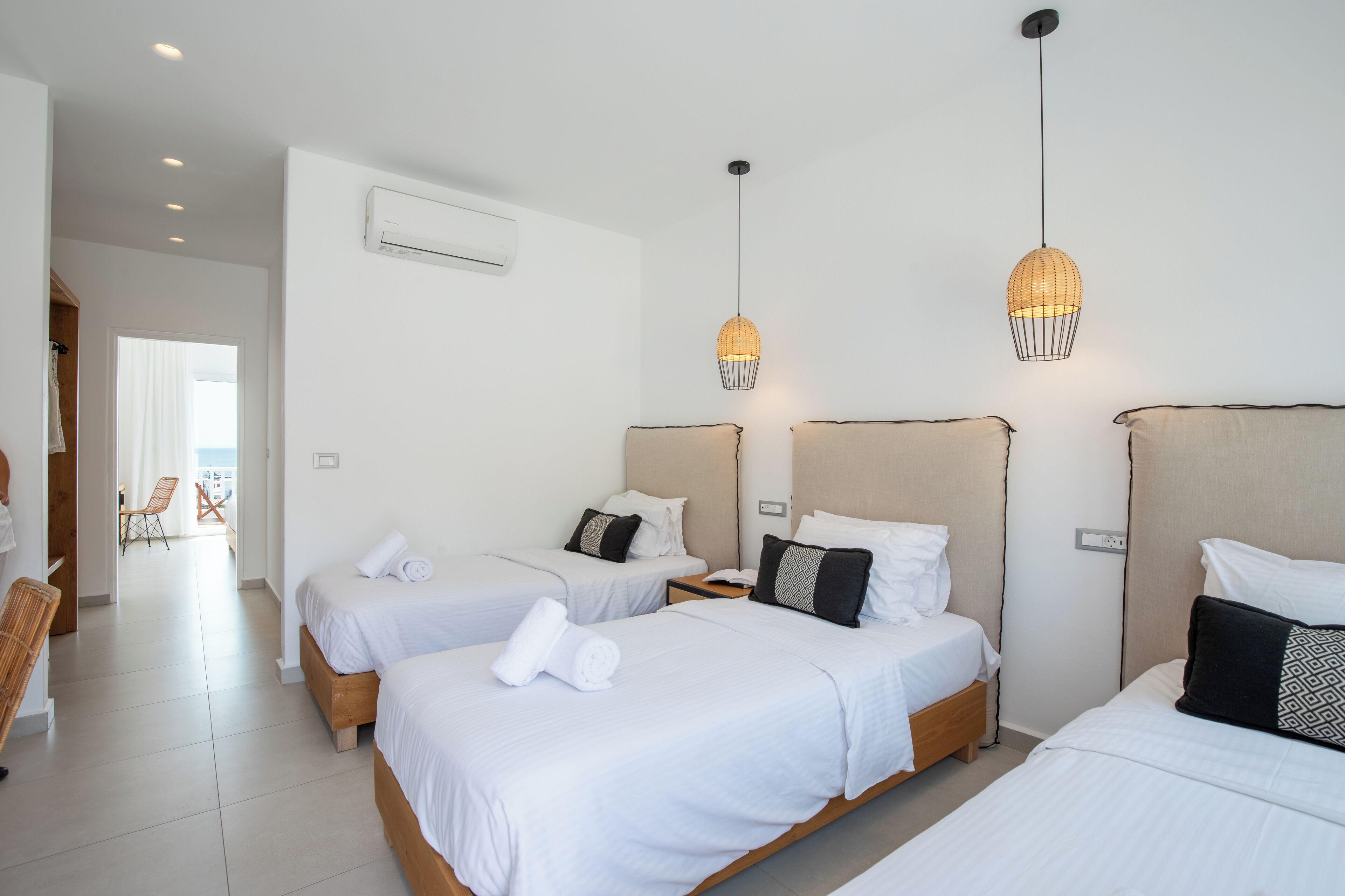 Habitación de hotel con tres camas, un área de descanso con una silla y vista al mar.
