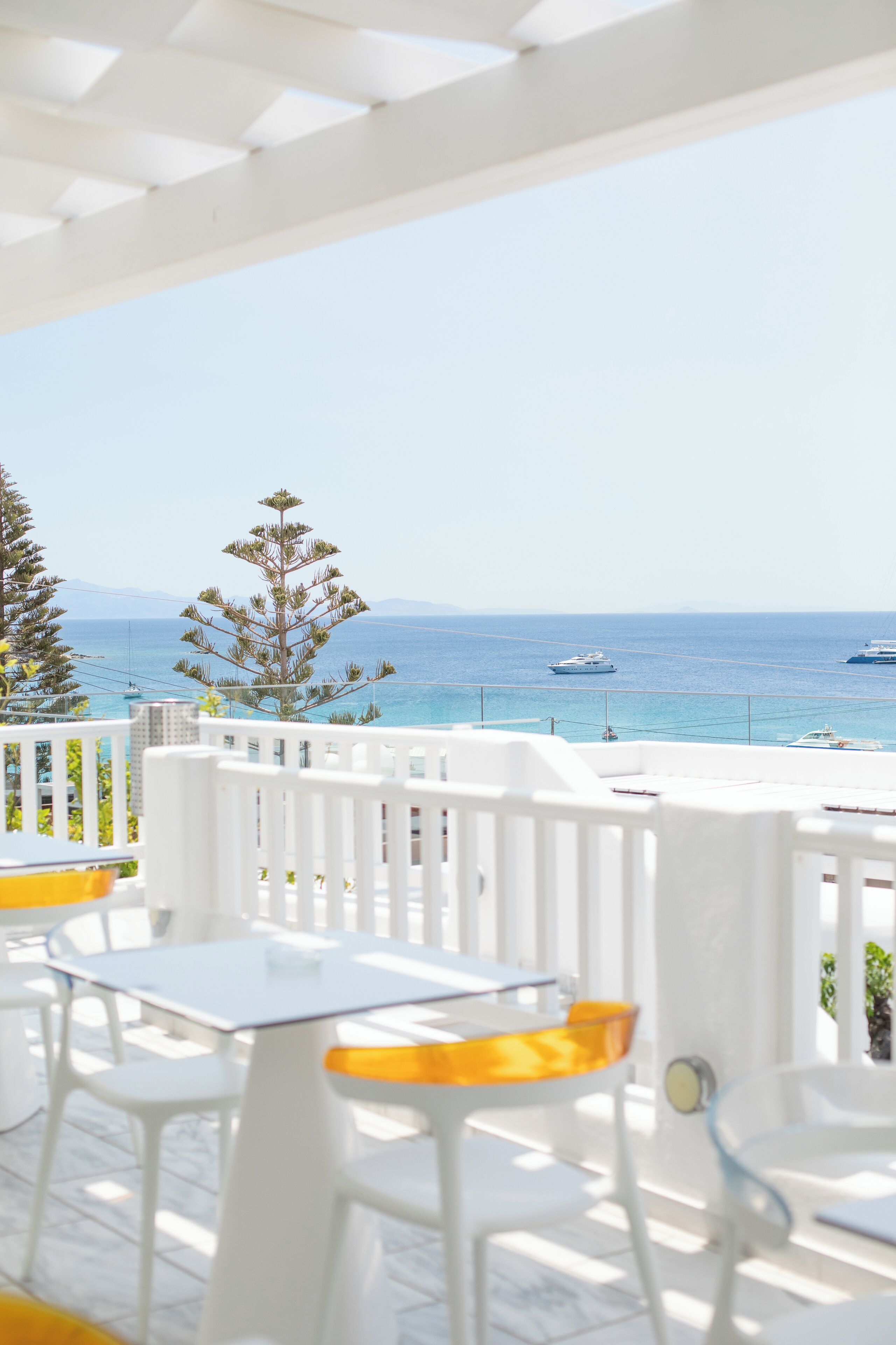 A terrace with white furniture, a view of the sea, and a tree.