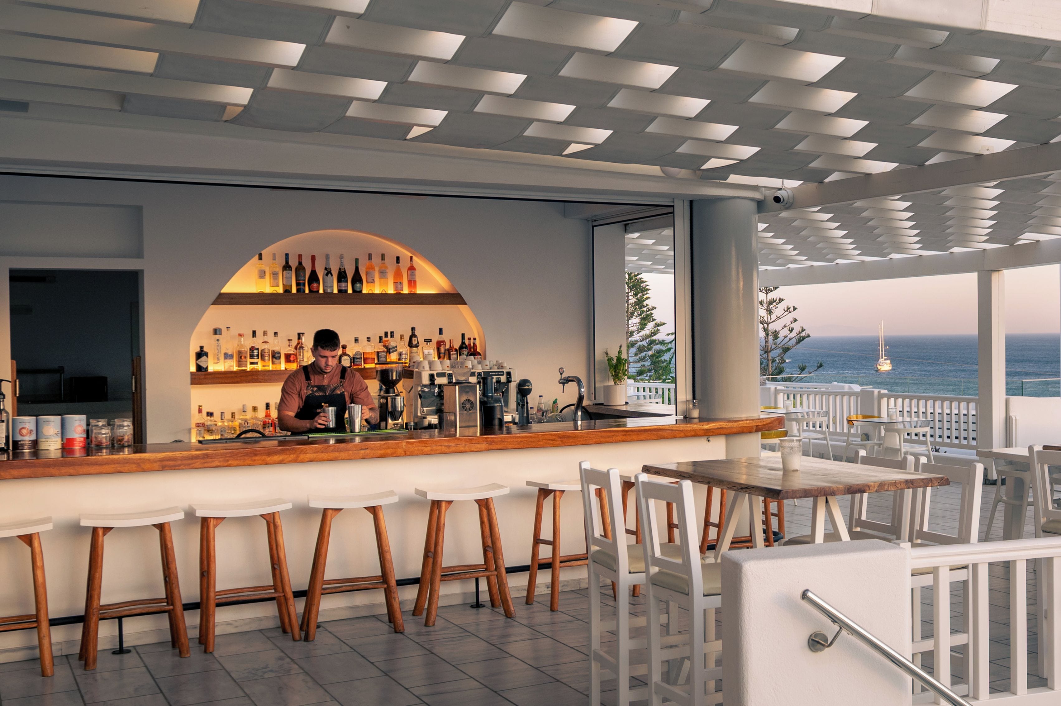 Un espace bar avec un barman, un assortiment de bouteilles et une vue sur la mer.