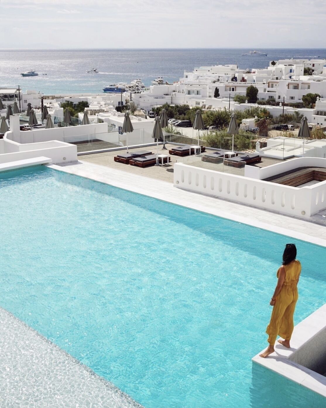 A pool with a view of white buildings and boats on the sea.