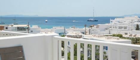 A balcony with a view of the sea, a chair, and two sunbeds with towels.