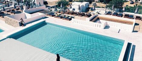 Una gran piscina con una persona caminando por el borde, rodeada de edificios blancos y vista al mar.