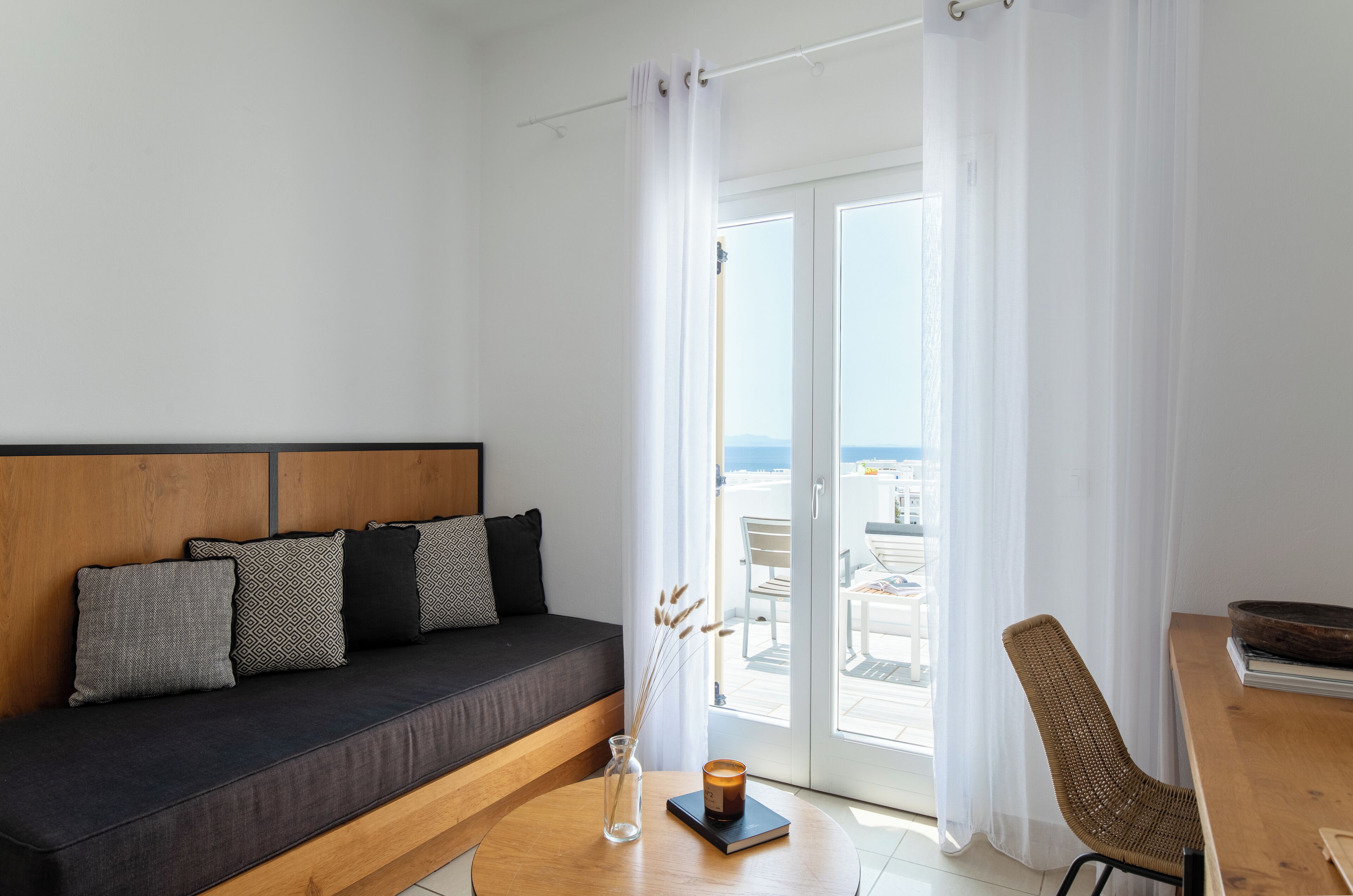 A modern living room with a dark sofa, patterned cushions, a wooden coffee table, and a view of the outdoors through a glass door.