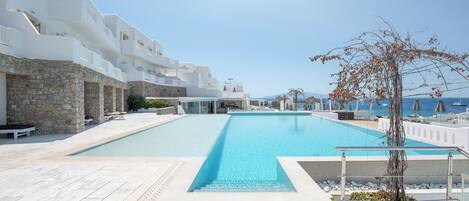 A swimming pool with a stone wall on one side and a white building with balconies on the other.