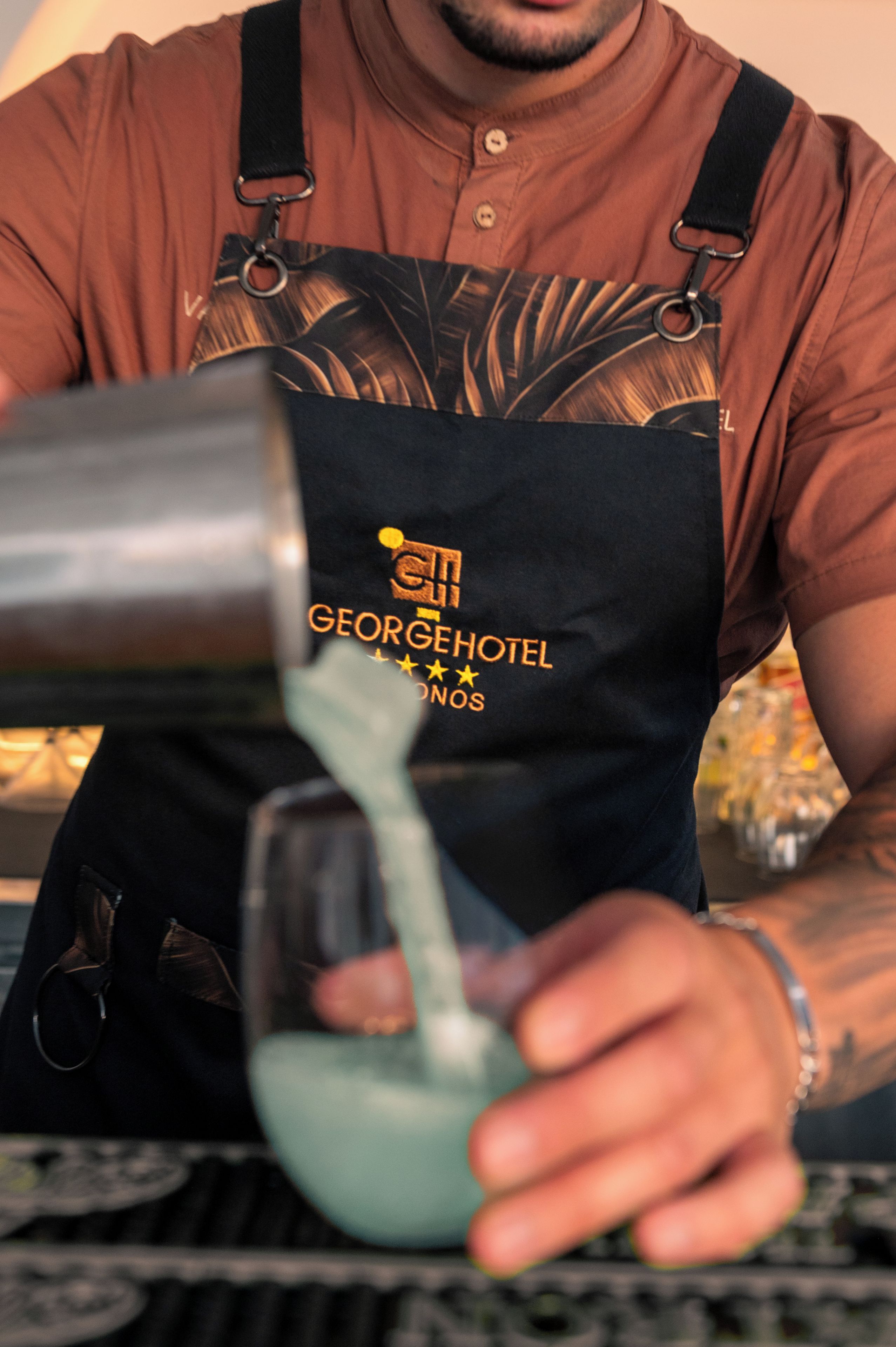 A person wearing a black apron with a logo, pouring a liquid into a glass.