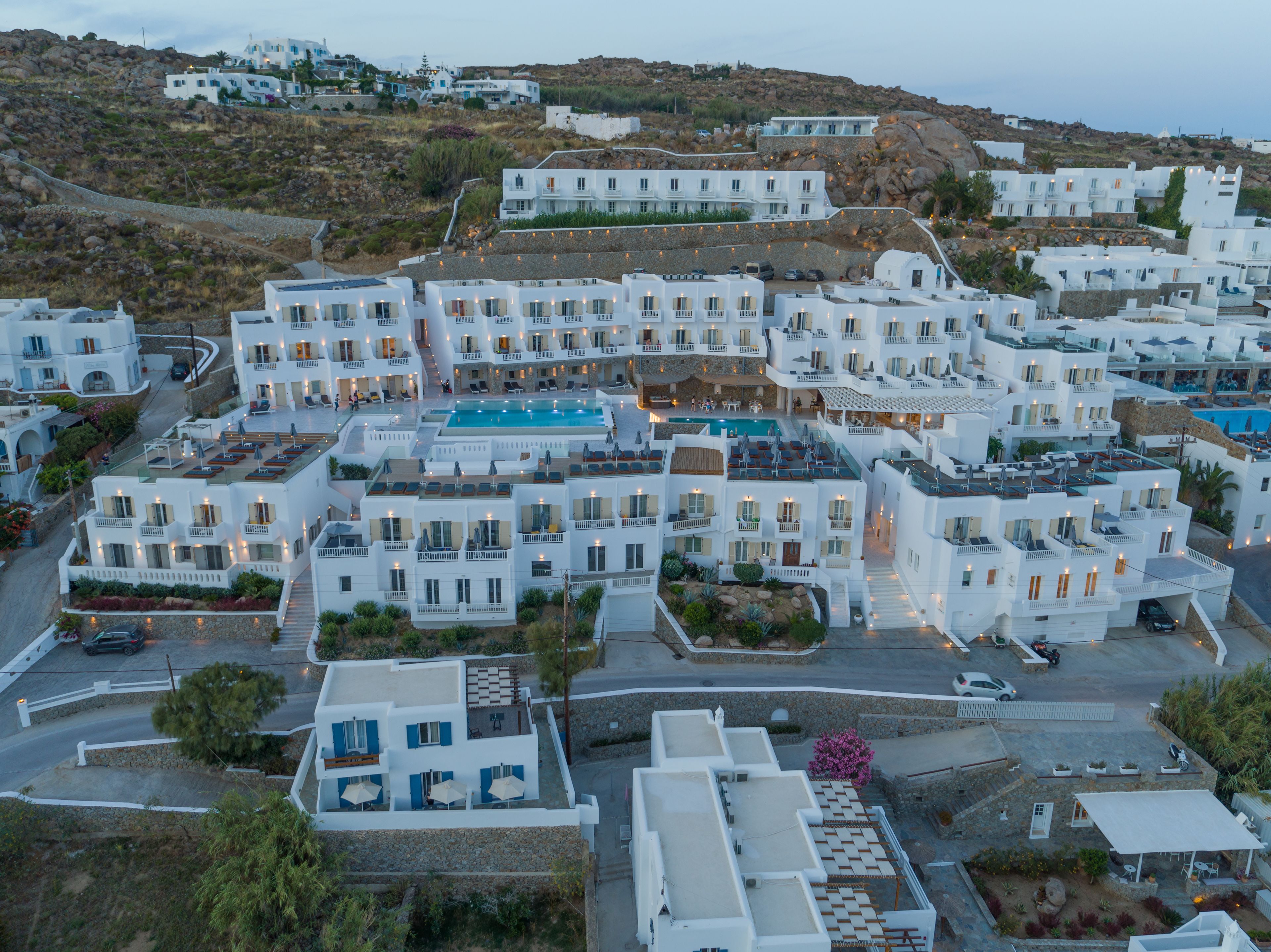 Un complejo turístico frente al mar con edificios blancos, piscina y un paisaje montañoso.