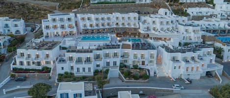 Un complejo turístico frente al mar con edificios blancos, piscina y un paisaje montañoso.