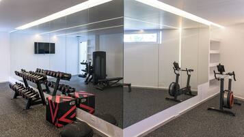 Un gimnasio con equipo de ejercicio, un televisor y un espejo.