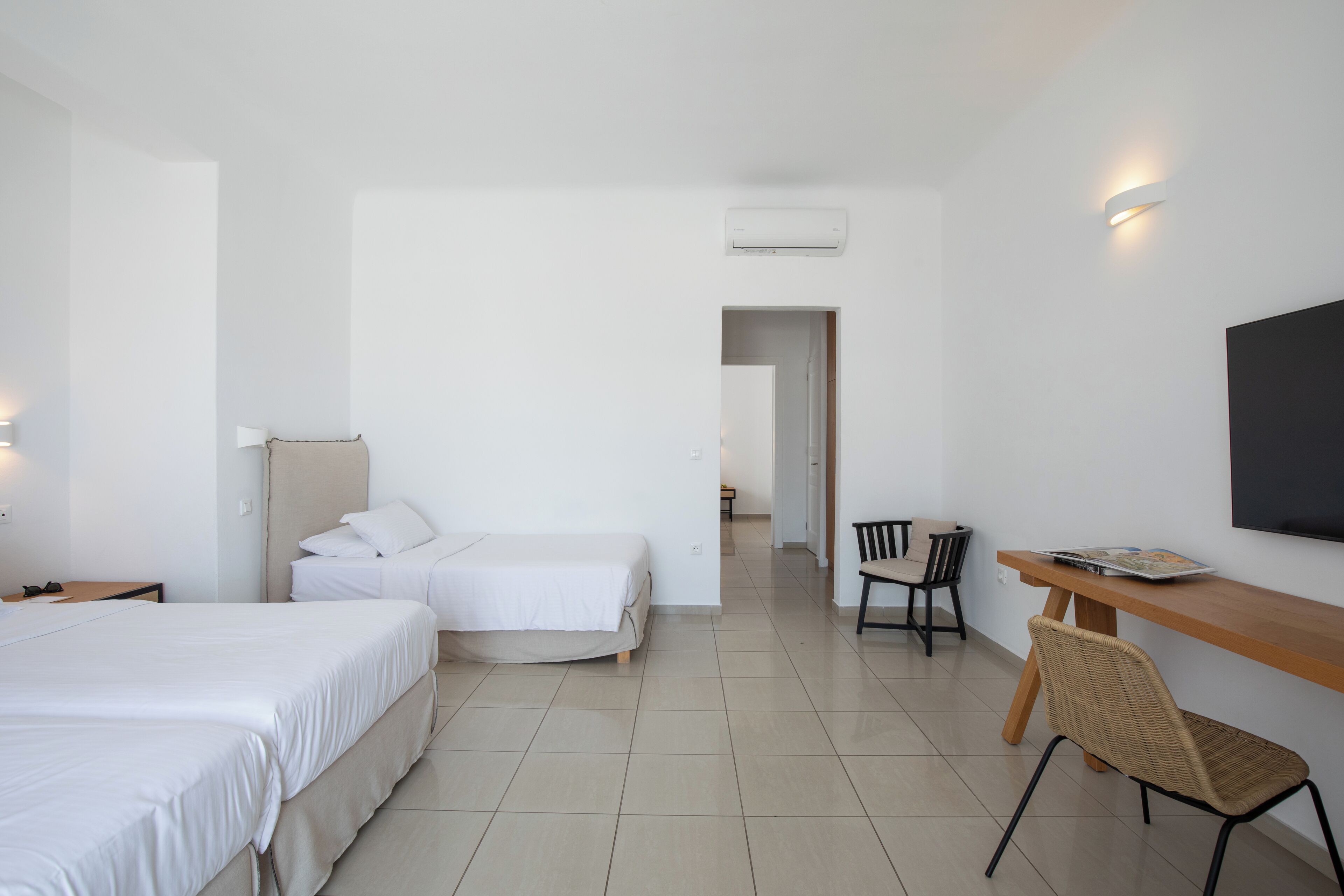 Camera d'albergo con due letti, una scrivania, una sedia, una TV e un condizionatore d'aria.