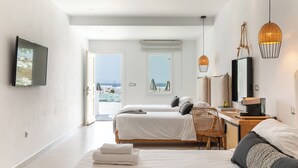 A modern hotel room with two beds, a desk, and a view of the sea. - The George Hotel (Mykonos)