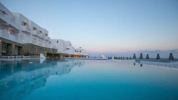 A poolside view of a resort with a clear sky, a pool, and a building with balconies. - The George Hotel (Mykonos)