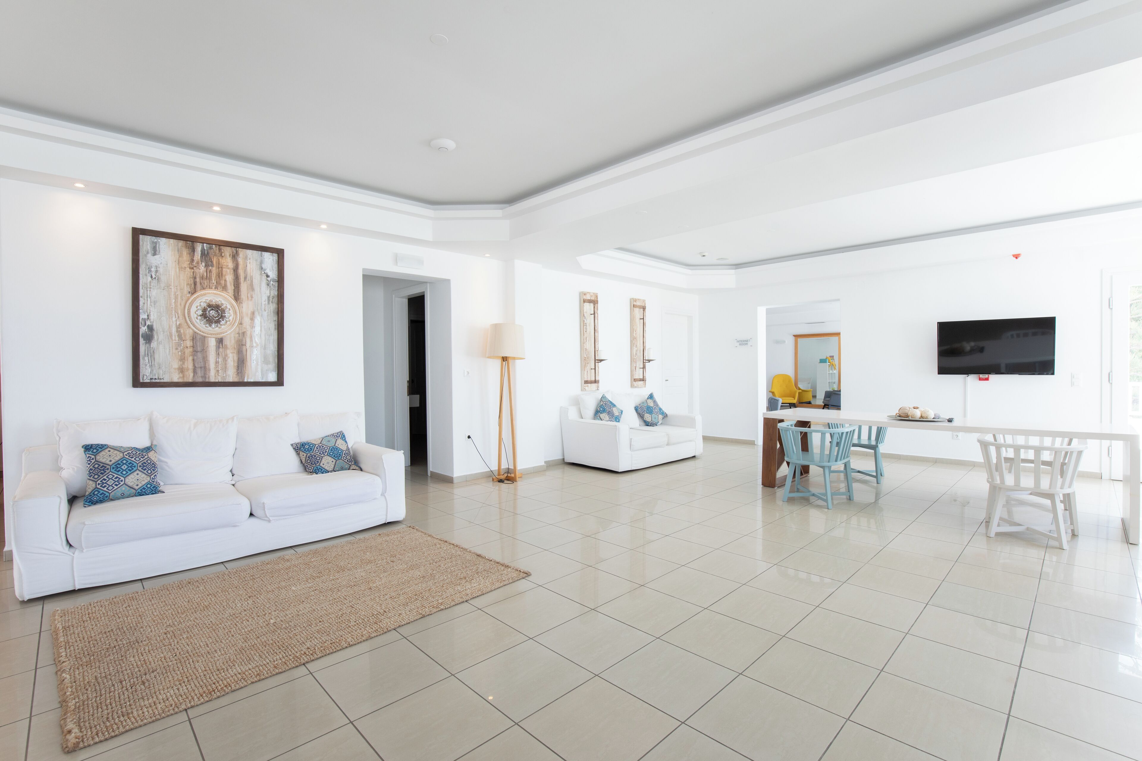 A spacious living area with a white sofa, a coffee table, and a TV mounted on the wall.
