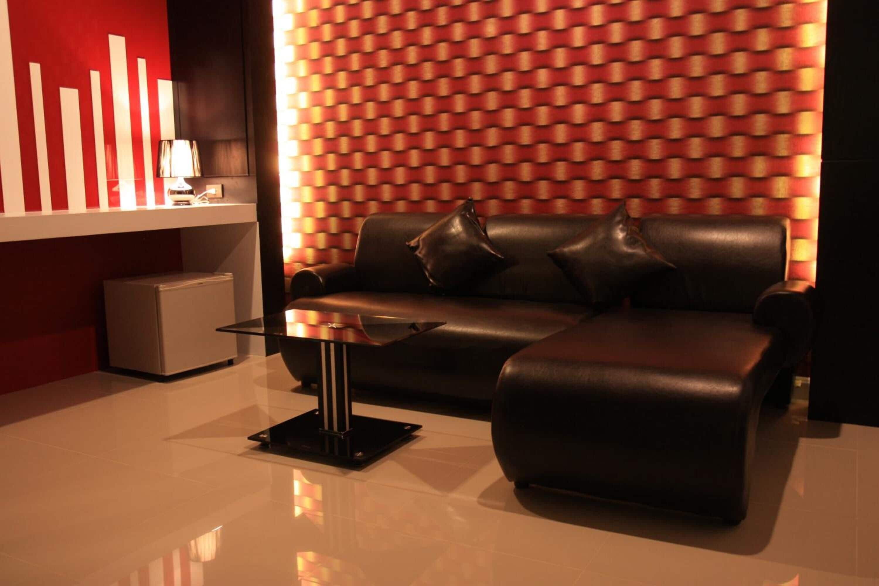 Una sala moderna con un sofá de cuero negro, una mesa de centro de vidrio y una pared con estampado rojo.
