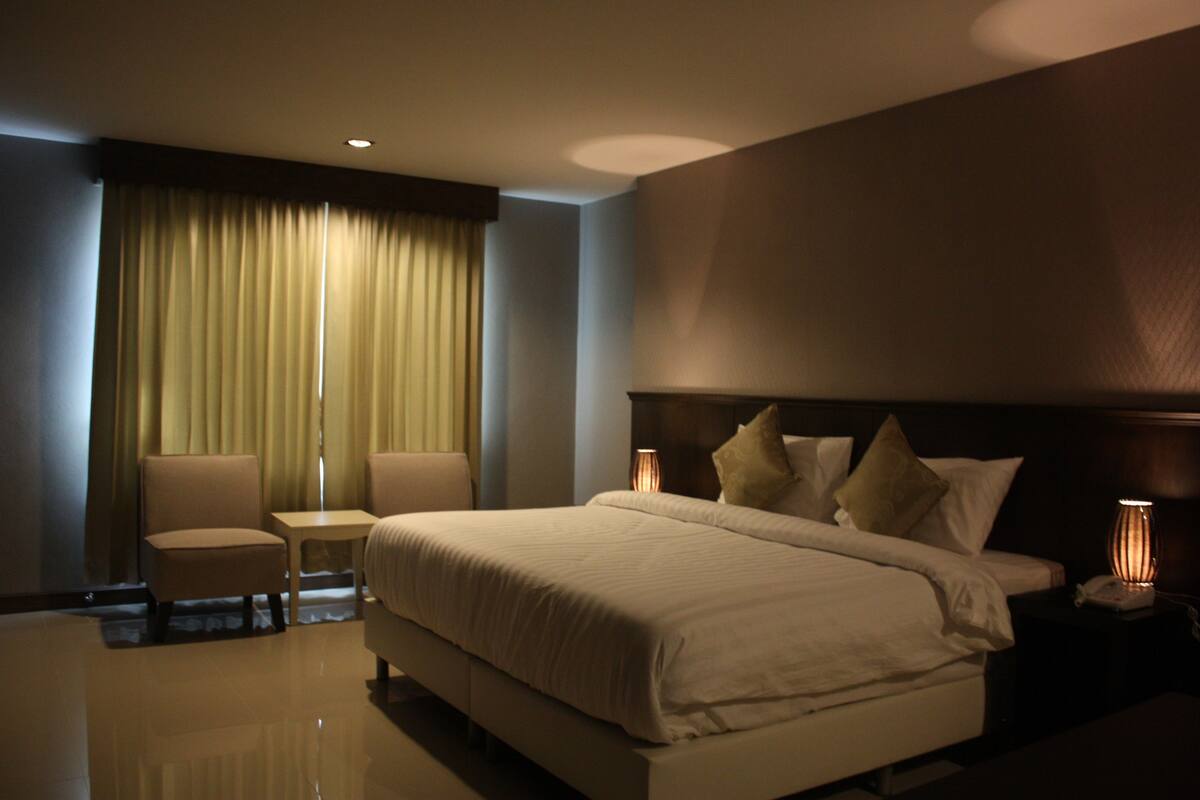 A hotel room with a large bed, two bedside tables, a chair, and a window with curtains.
