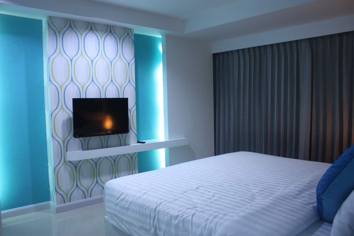 A modern hotel room with a large bed, a flat-screen TV mounted on a wall with a geometric pattern, and a window with curtains.
