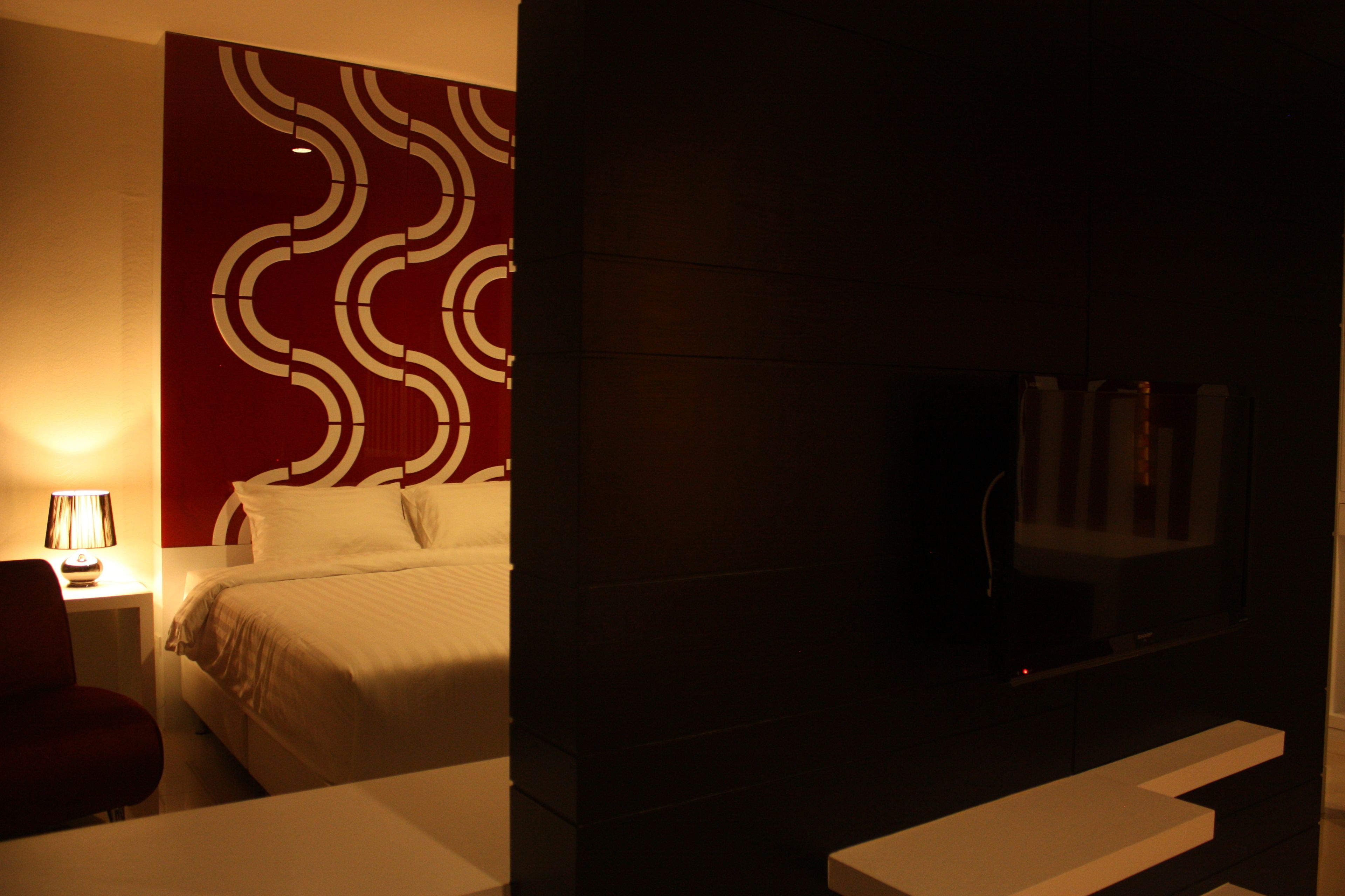 A hotel room with a bed, a TV, a lamp, and a wall with a geometric pattern.