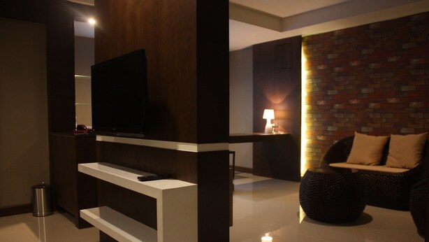 Een moderne woonkamer met een flatscreen televisie bevestigd aan een wit tv-meubel, een muur met een bakstenen patroon, een donkergrijze bank met kussens en een kleine tafel met een lamp.