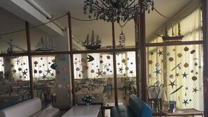 A room with a white sofa, a blue armchair, and a small table. There are starfish and shells hanging from the ceiling. - Hotel Lux (Cesenatico)