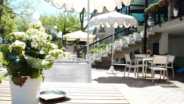 A patio area with a white potted plant, outdoor seating, and a staircase leading to an upper level. - Hotel Lux (Cesenatico)