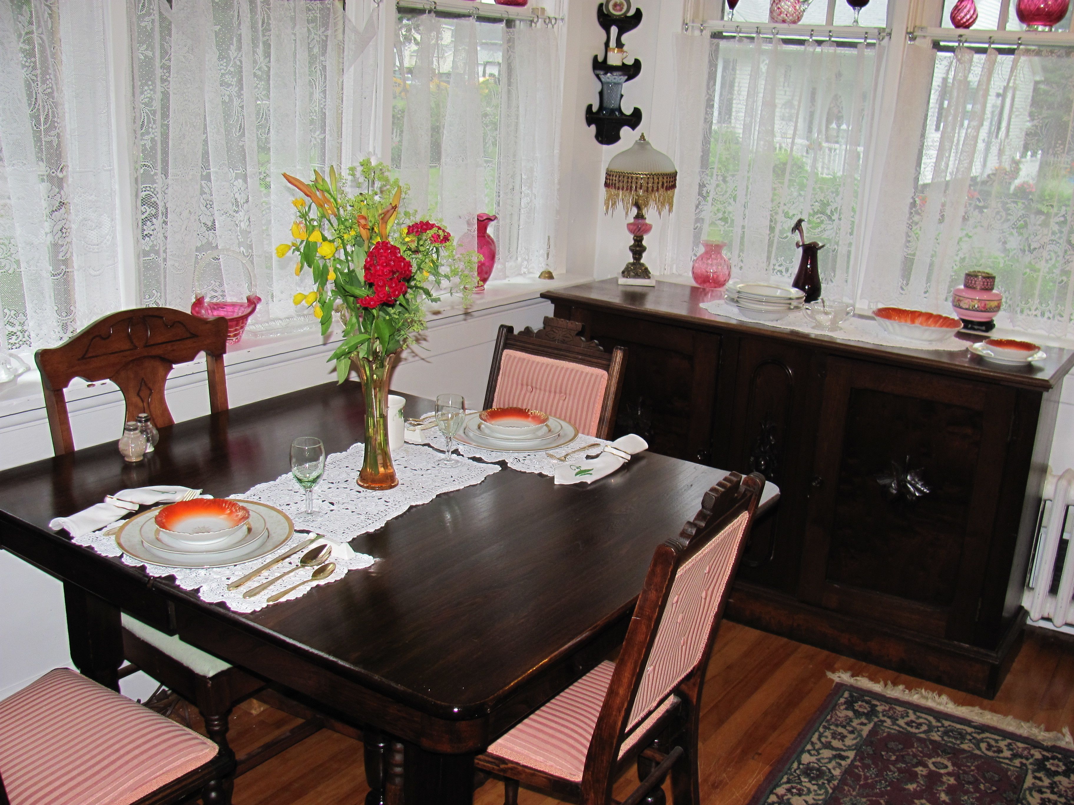 A dining room with a wooden table set for four, chairs, a vase of flowers, and a cabinet with decorative items.