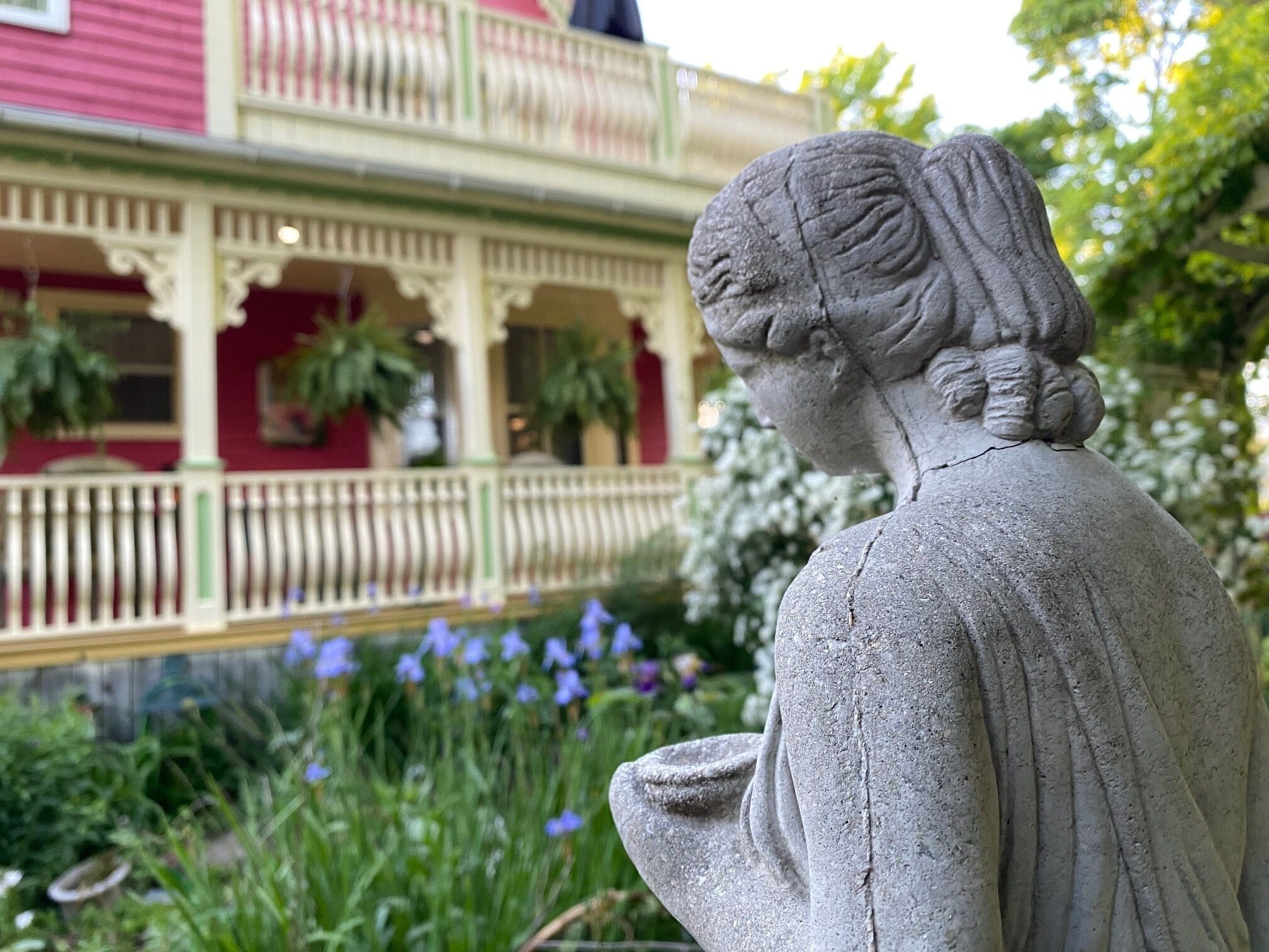 A statue of a woman in a garden with a building in the background.