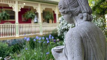 A statue of a woman in a garden with a building in the background.