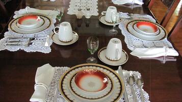 Mesa de comedor formal con vajilla, cubiertos y cristalería blancos y dorados.