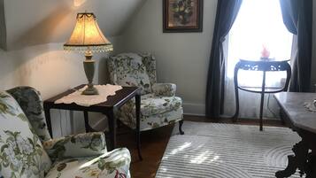 Una sala de estar con muebles de estampado floral, una mesa con mantel de encaje, una lámpara y un cuadro en la pared.