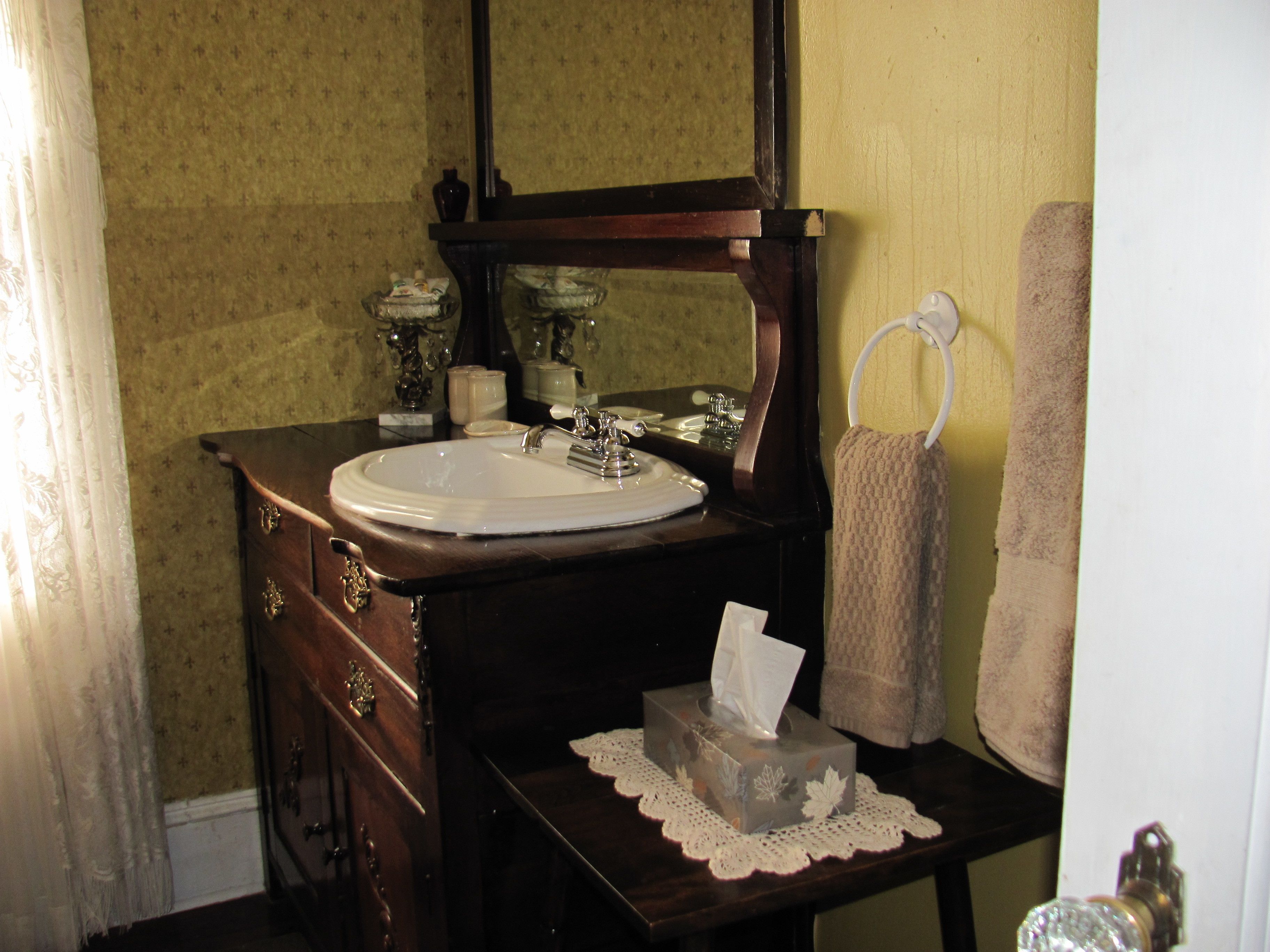A bathroom with a wooden vanity, a white sink, a mirror, and a towel rack.