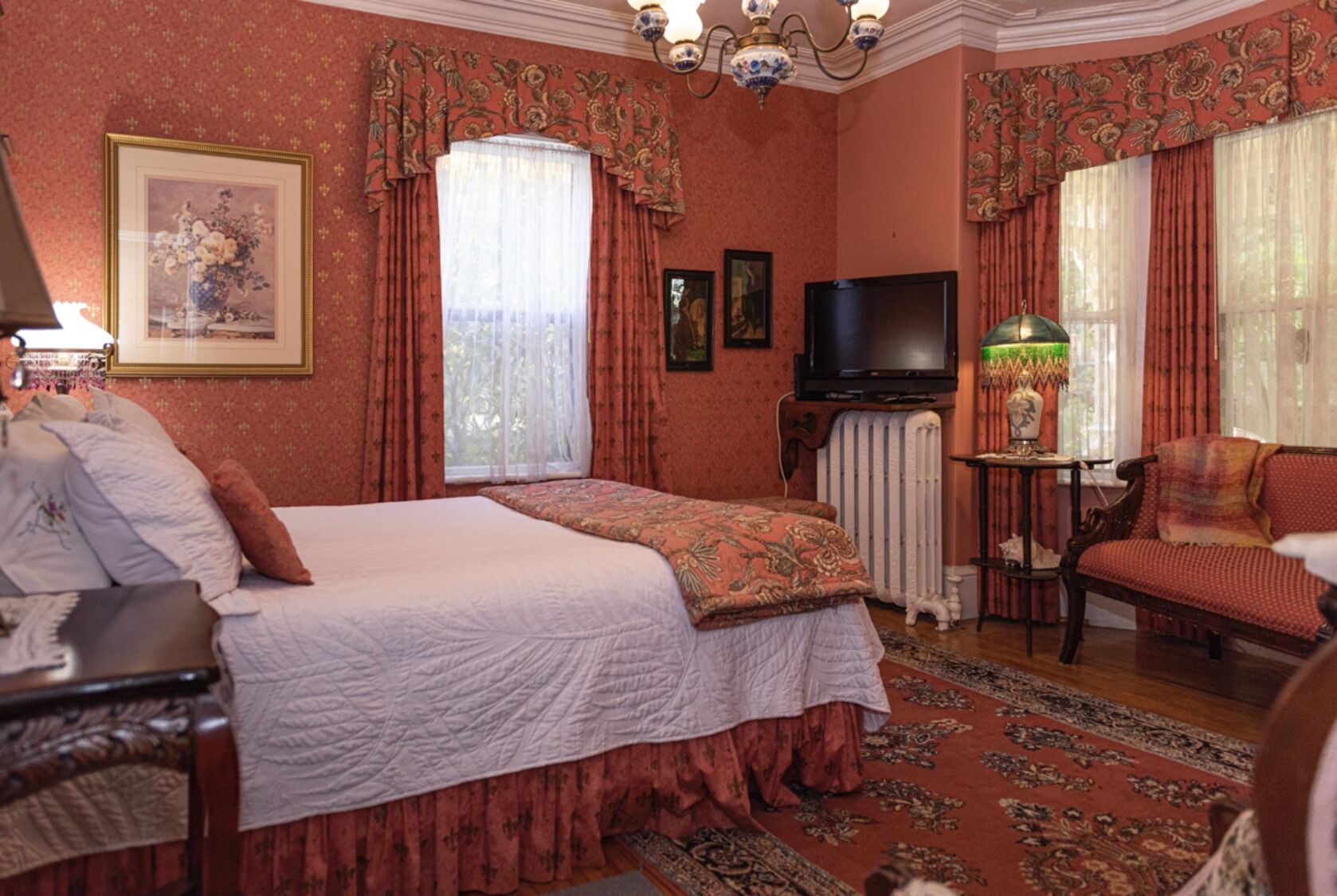 Een klassieke kamer met een bed, televisie, stoel en een tafel met lamp.
