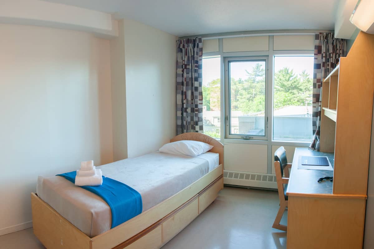 Un dormitorio pequeño y ordenado con una cama individual, un escritorio y una ventana con cortinas.