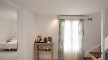 A hotel room with a bed, a wooden side table with a coffee maker, cups, and a picture frame. There is a staircase with wooden steps and a striped curtain.