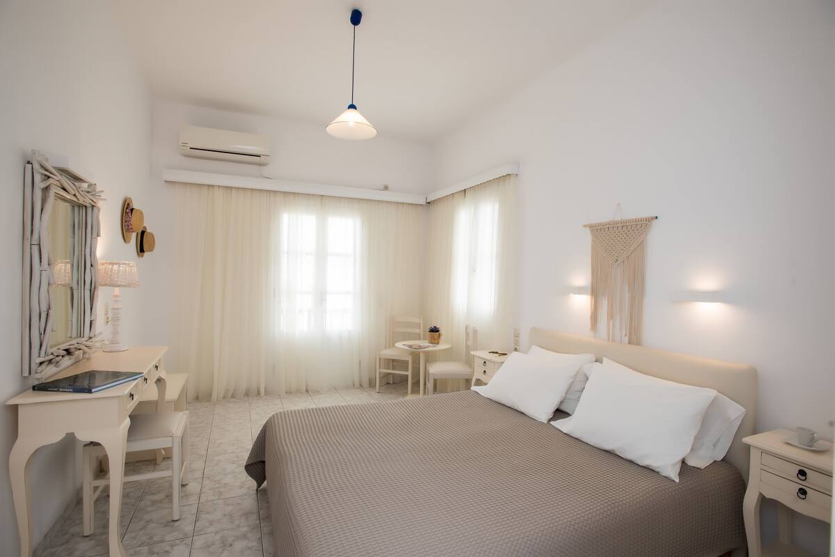 A hotel room with a bed, bedside tables, a desk with a chair, a mirror, and a hanging light fixture.