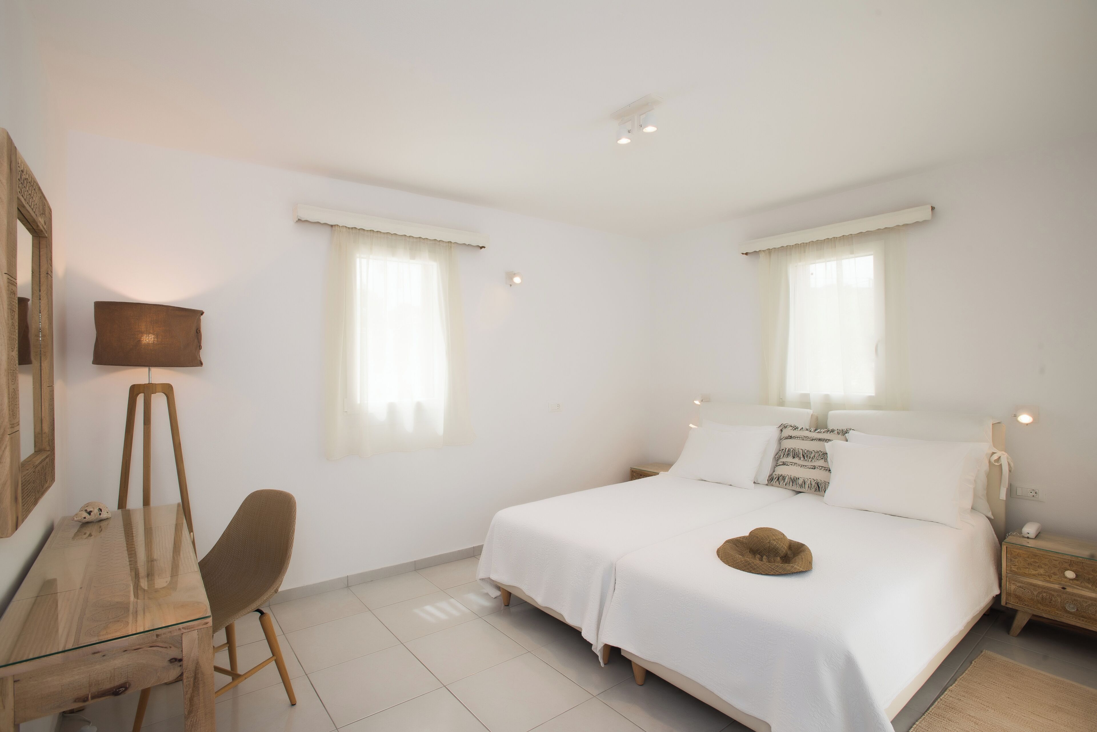 A bedroom with a bed, a desk, a chair, a lamp, and two windows with curtains.