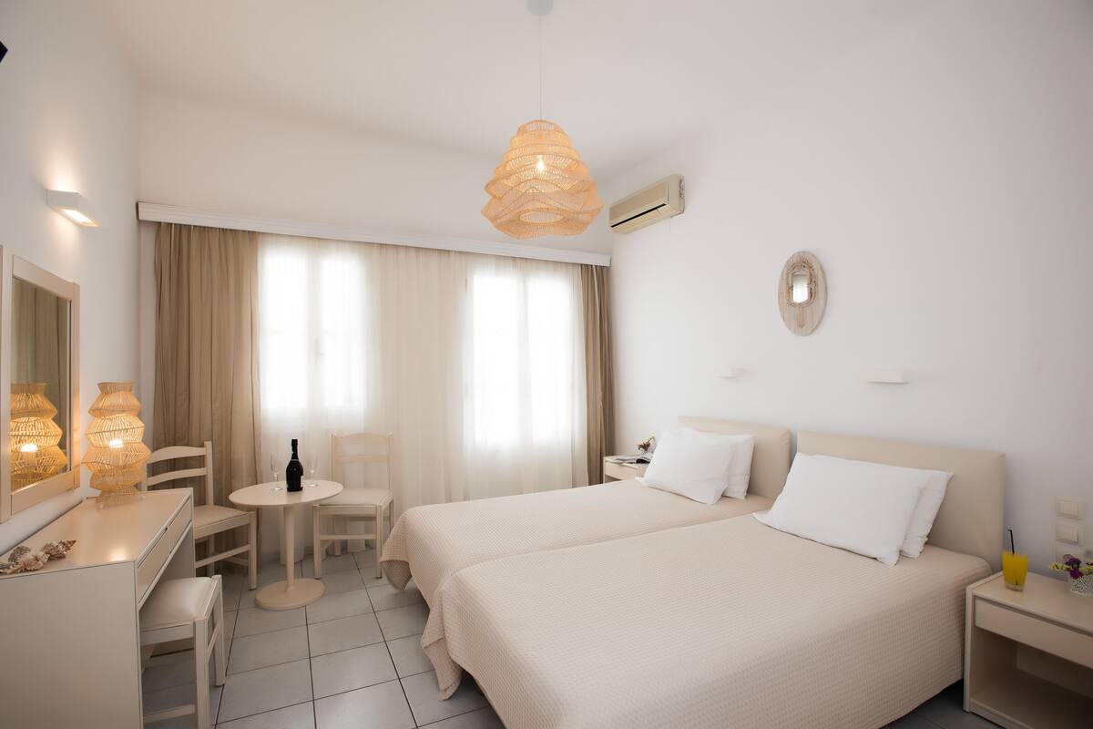 A hotel room with two beds, a desk, a chair, a small table, and a hanging light fixture.