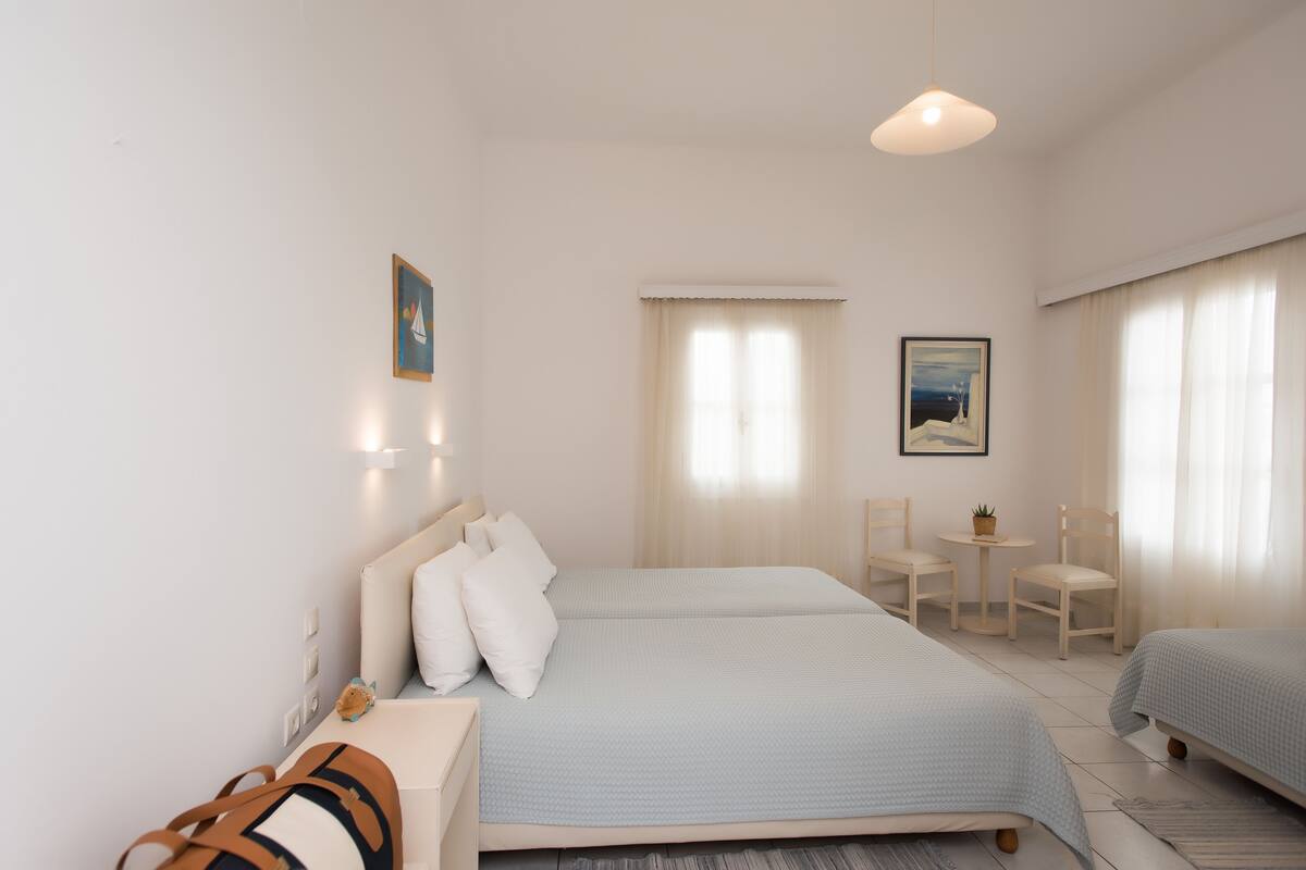 A hotel room with two beds, a desk, chairs, a small table, and a potted plant.