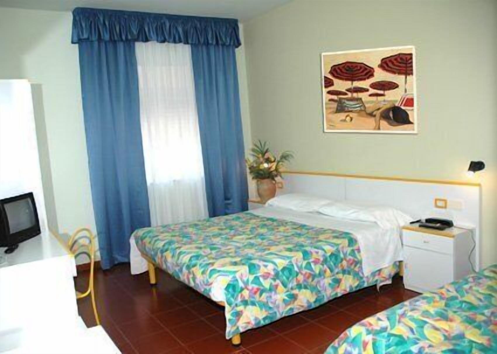 Una camera d'albergo con due letti, una scrivania, una sedia, una televisione e un quadro appeso al muro.